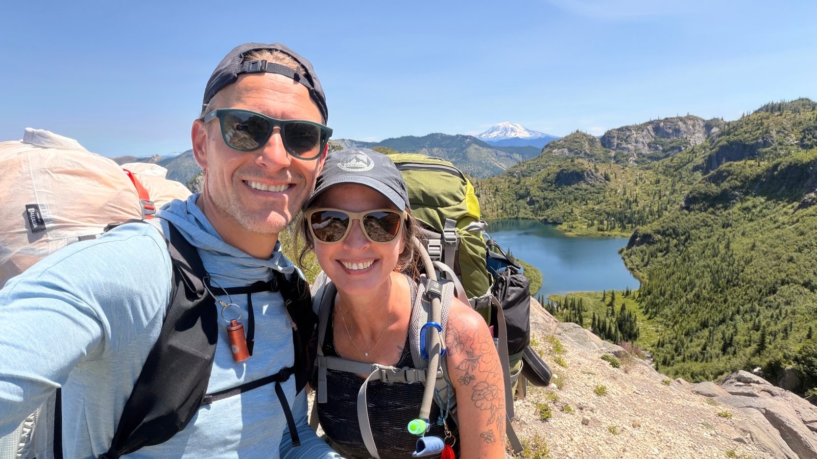 Jarod and Rachel smiling together with backpacks above a mountain lake
